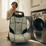 A woman holding a car seat cover in front of a modern dryer, wondering — can you put car seat covers in dryer ?