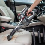 Home 18 Person using the best affordable vacuum cleaner for car​ to clean crumbs from beige car seats.